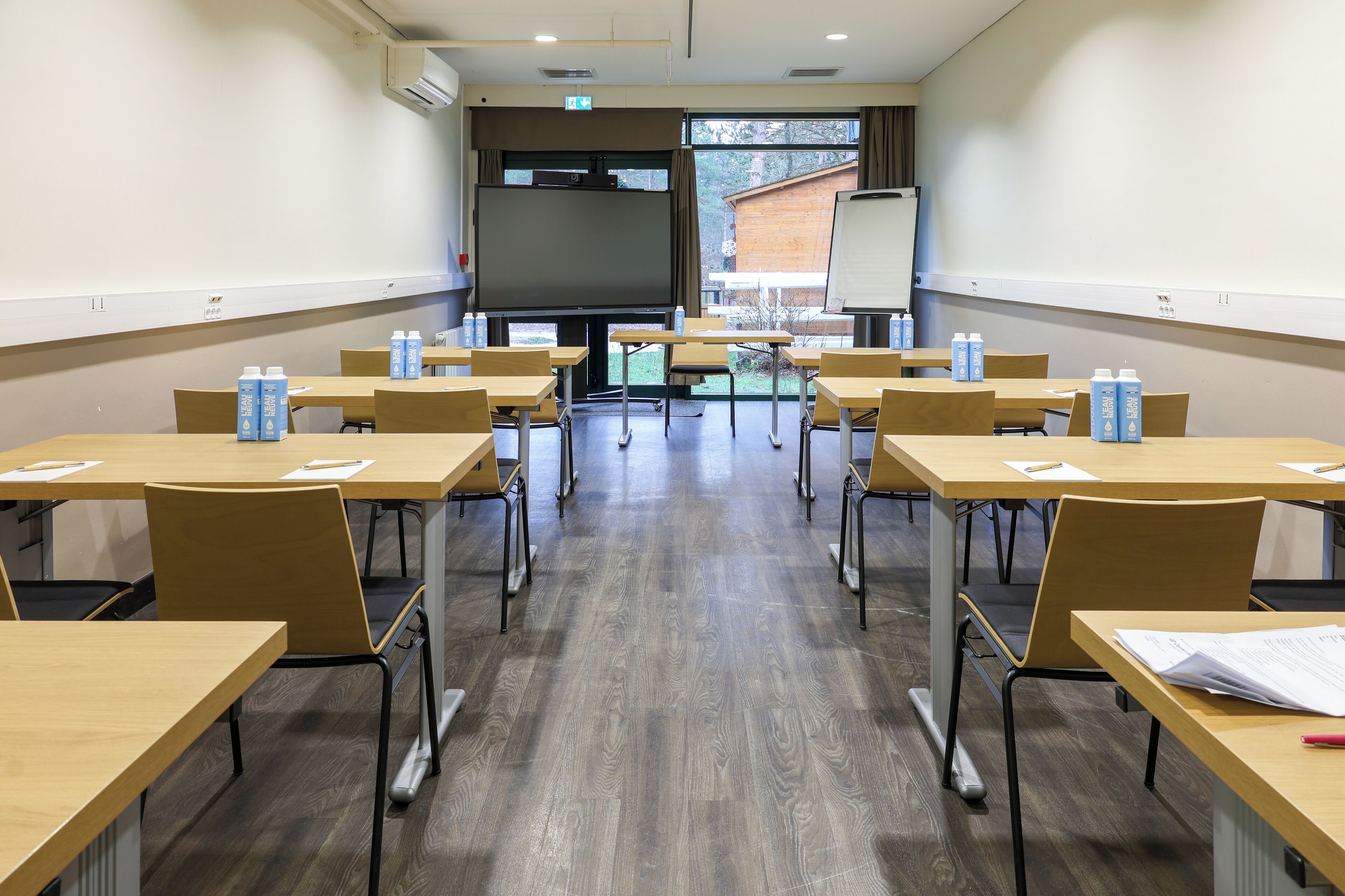 A classroom with wooden desks, chairs, and a large screen at the front.