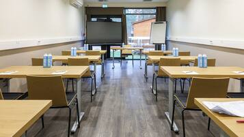 A classroom with wooden desks, chairs, and a large screen at the front.