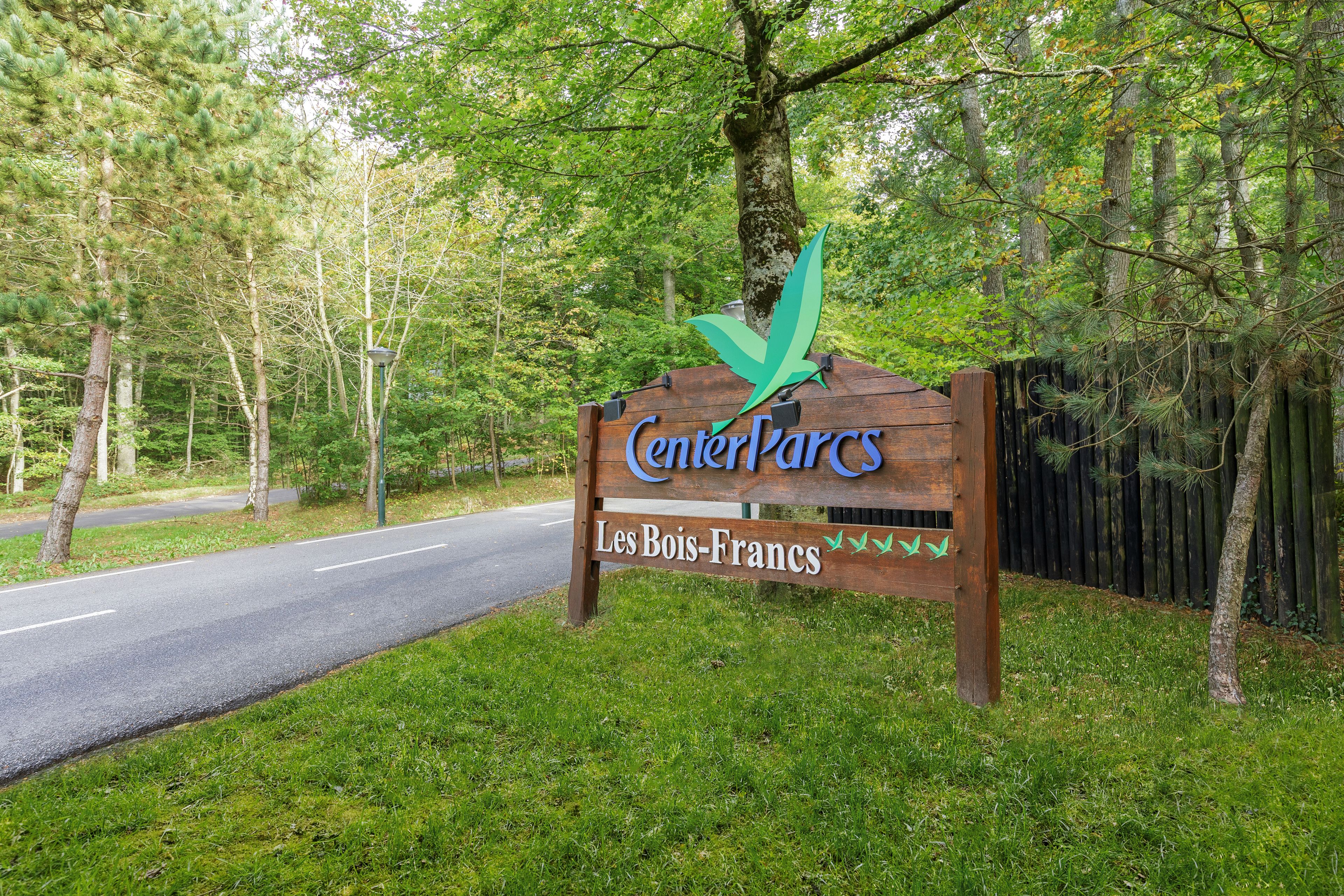 A wooden sign with the text "CenterParcs Les Bois-Francs" and a green arrow pointing upwards.