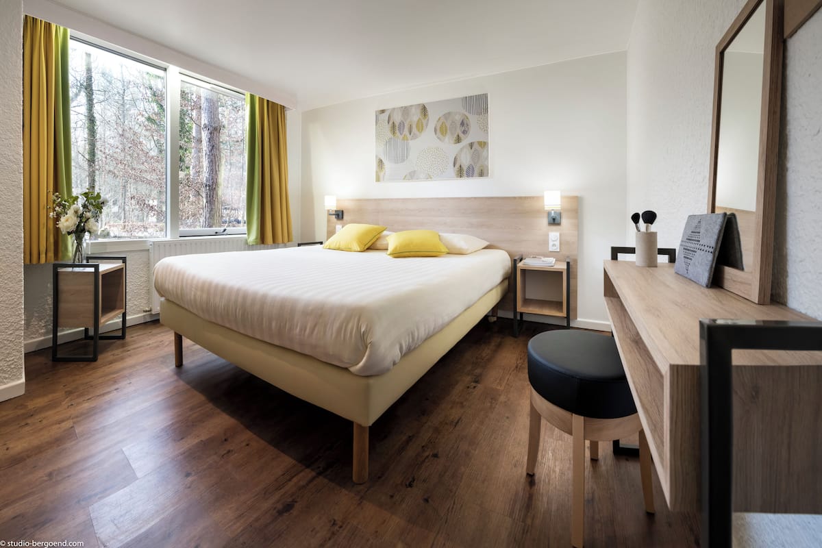 Ein modernes Hotelzimmer mit einem großen Bett, Nachttischen, einem Schreibtisch und einem Fenster mit Vorhängen.