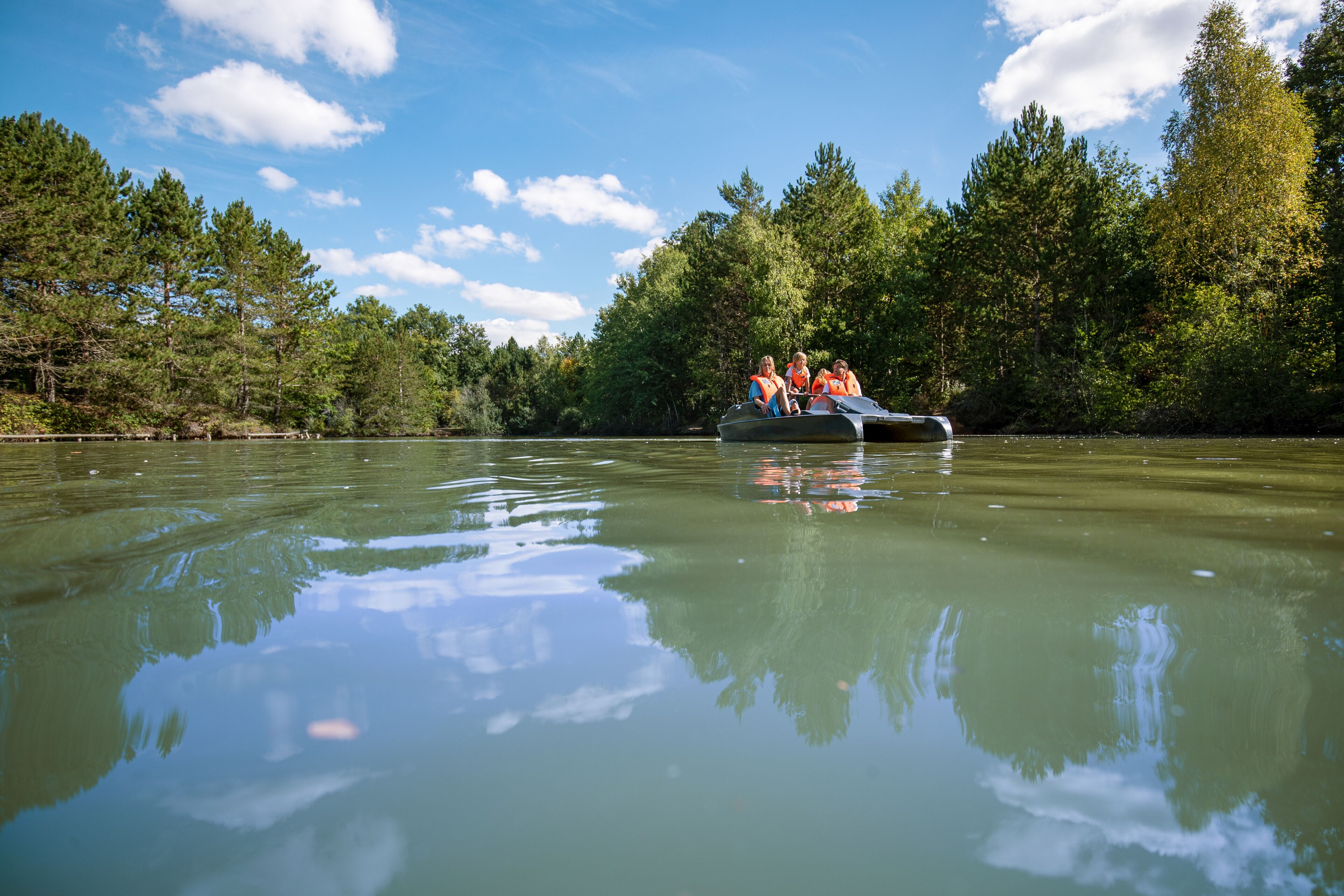 A group of people on a boat in a calm body of water surrounded by trees.