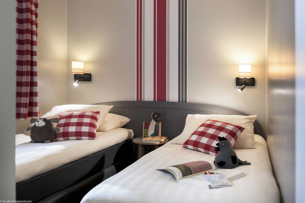 Ein Hotelzimmer mit zwei Betten, karierten Kissen, Wandleuchten und einem gestreiften Wanddesign.