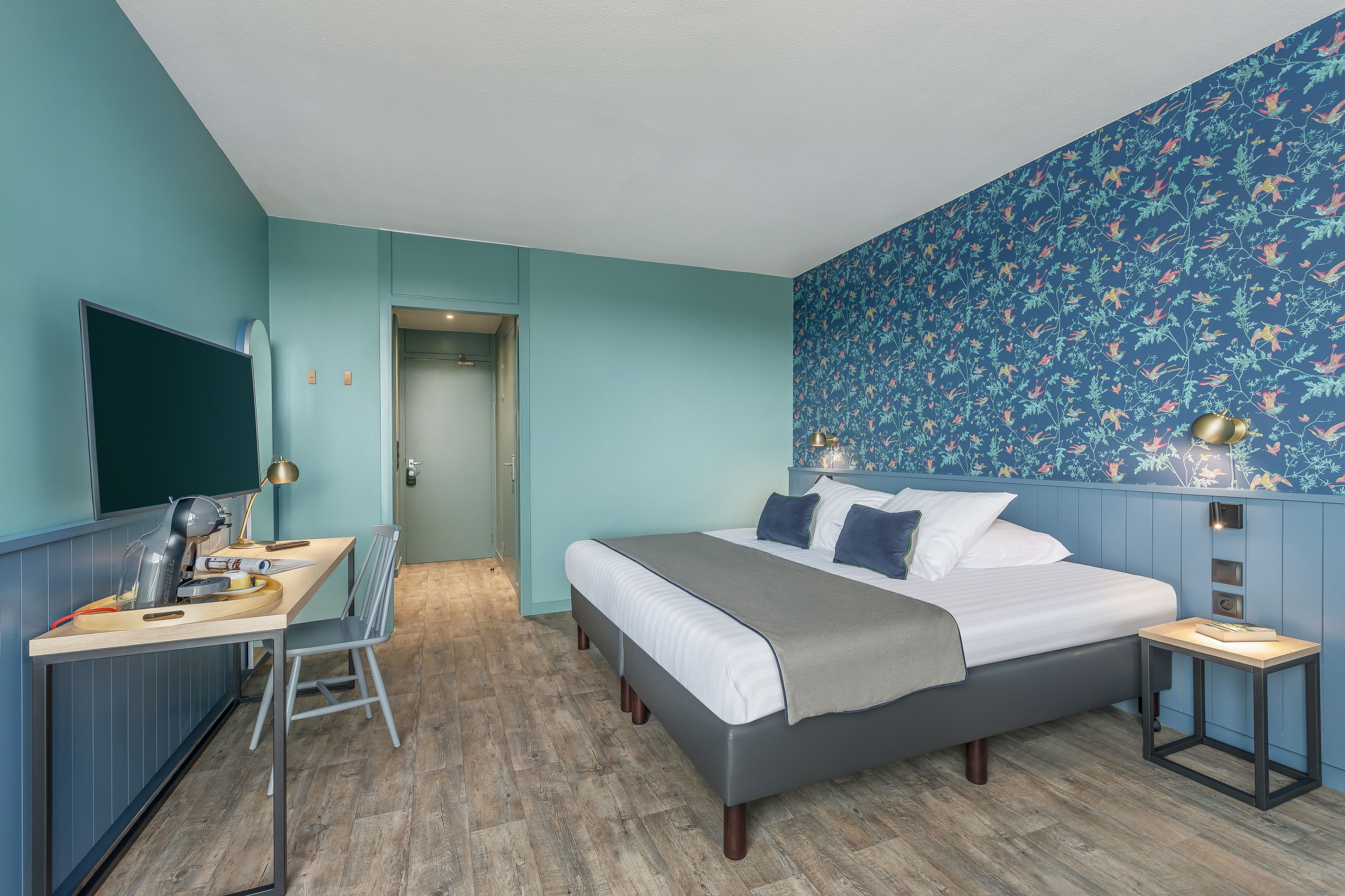 A bedroom with a bed, desk, chair, and a wall-mounted TV.