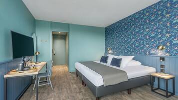 A bedroom with a bed, desk, chair, and a wall-mounted TV.