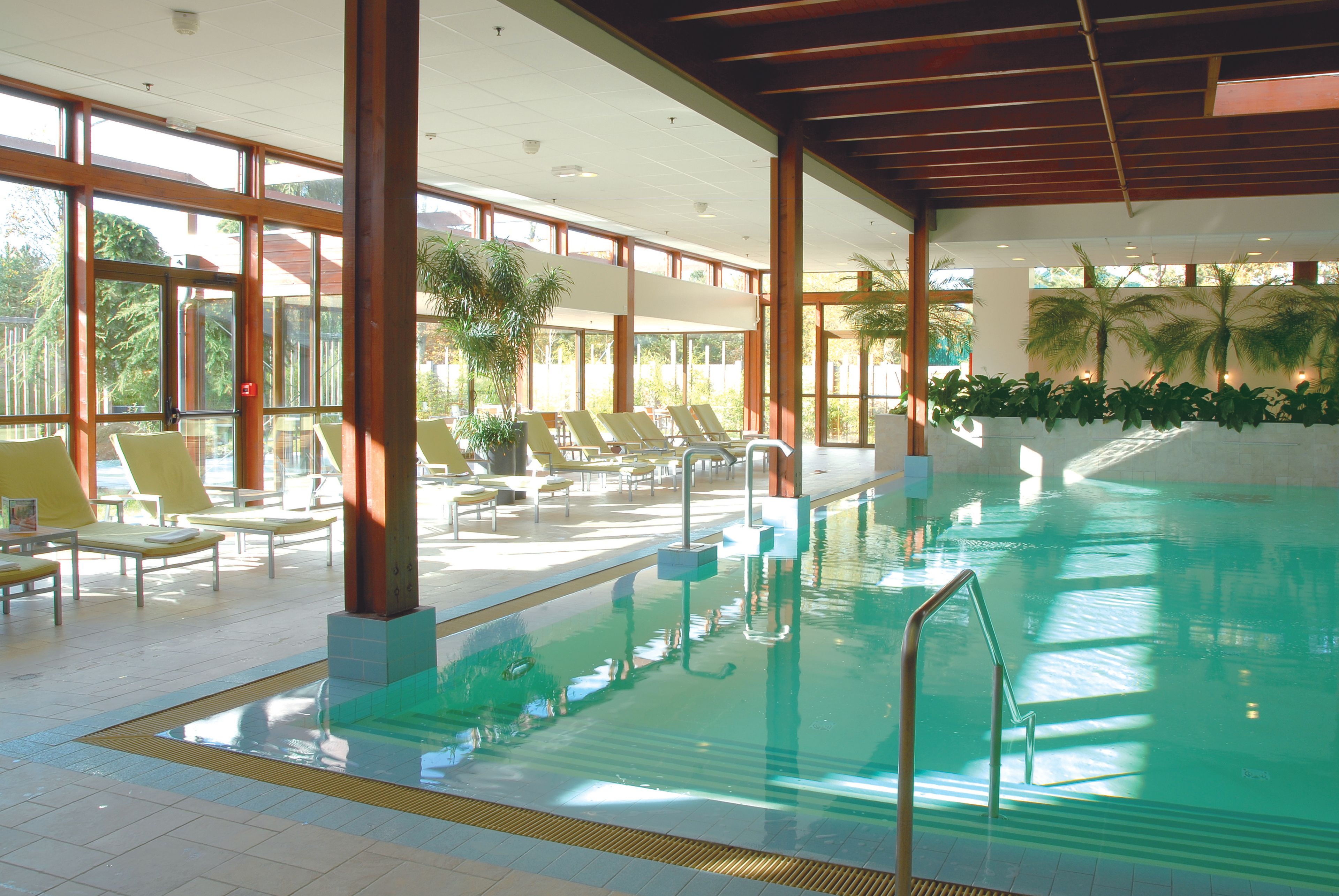 An indoor swimming pool with clear water, surrounded by sun loungers and large windows.