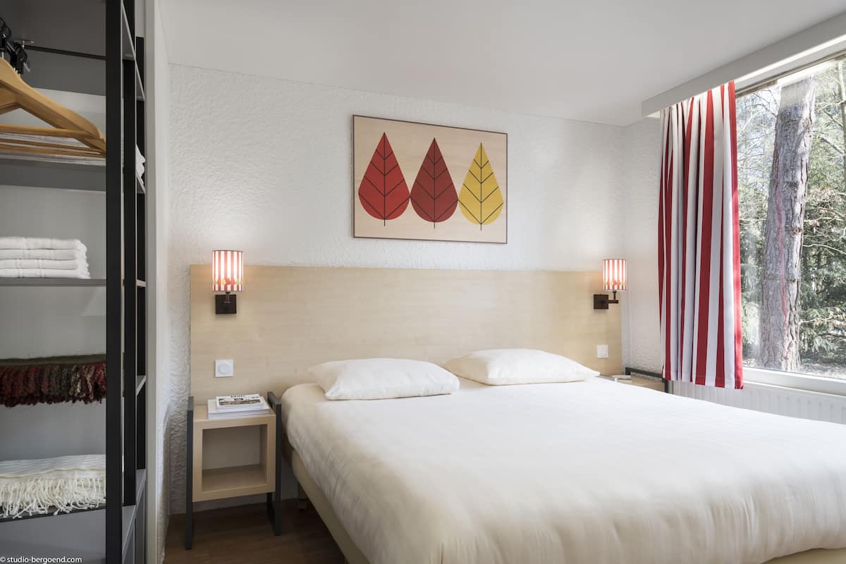 Ein Hotelzimmer mit einem Bett, zwei Nachttischen, einem Wandbild und einem Fenster mit Vorhängen.