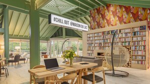 A cozy reading area with a wooden table, chairs, and a bookshelf filled with books. - Center Parcs Les Bois-Francs (Les Barils)