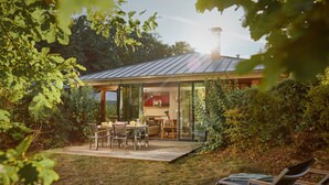 A modern house with a patio, a dining area, and a kitchen visible through glass doors. - Center Parcs Les Bois-Francs (Les Barils)
