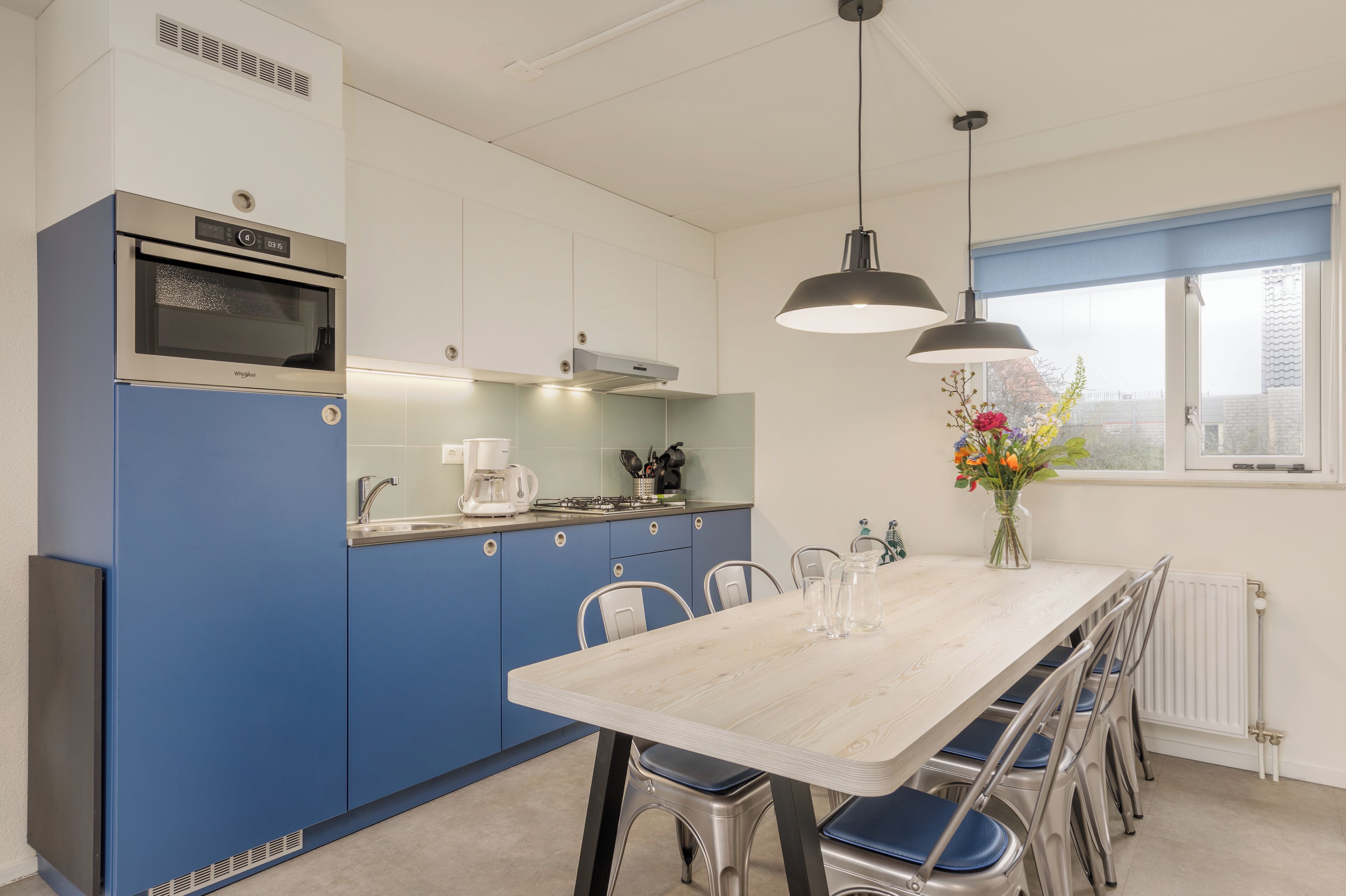 A modern kitchen with a built-in oven, a coffee maker, and a dining area with a table and chairs.