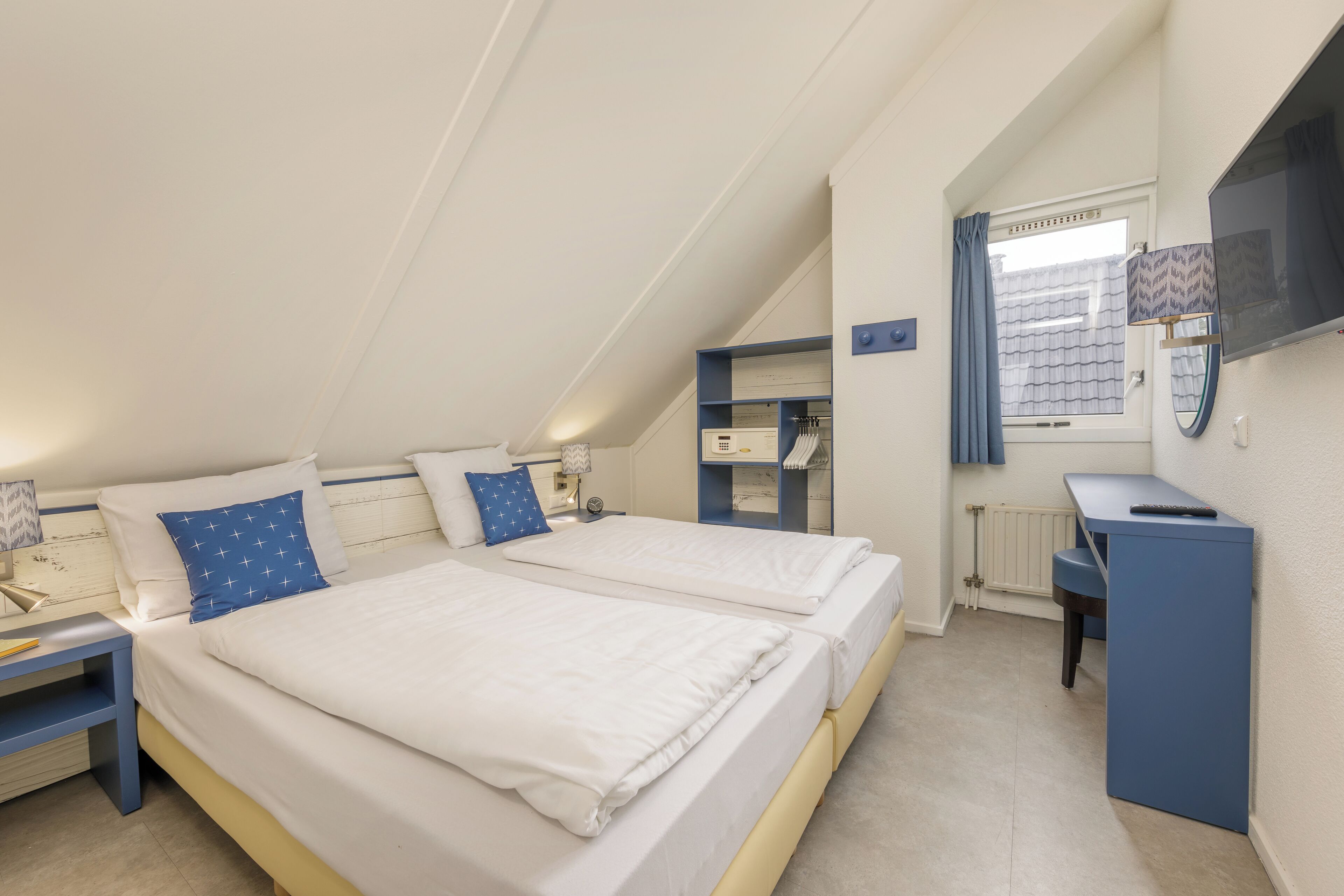 Ein Schlafzimmer mit zwei Betten, einem Schreibtisch und einem Fenster mit Vorhängen.