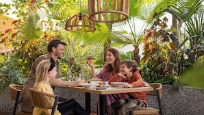 A family dining at an outdoor table surrounded by lush greenery and modern wicker chairs. - Center Parcs Zandvoort Beach (Zandvoort)
