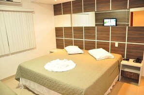 A hotel room with a bed, a bedside table with a phone, and a TV mounted on the wall. - Catú Palace Hotel (Rondonopolis)