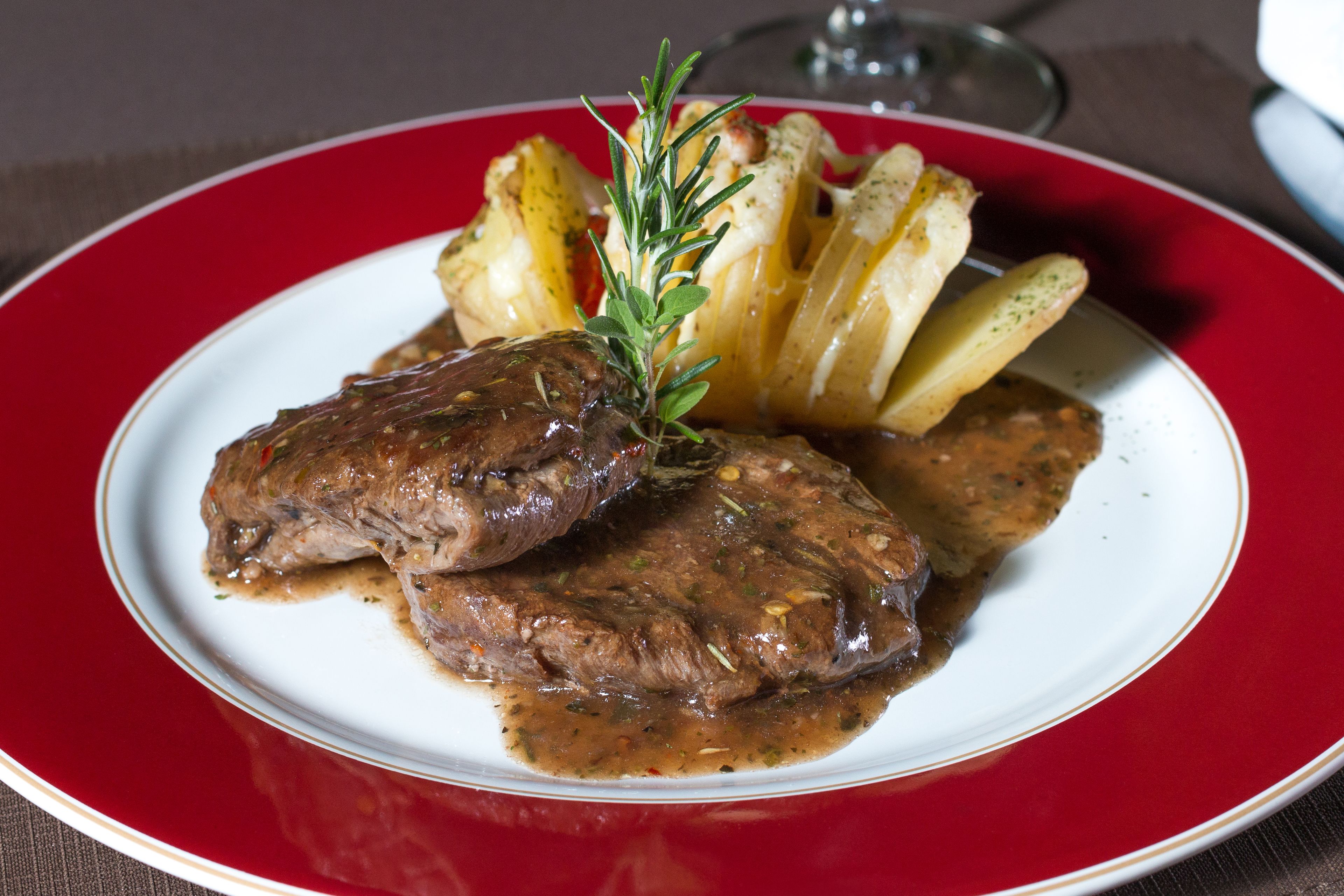 A plate with two pieces of meat, potatoes, and a sprig of rosemary.
