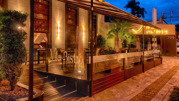 A restaurant with a glass facade, outdoor seating, and a well-lit entrance.