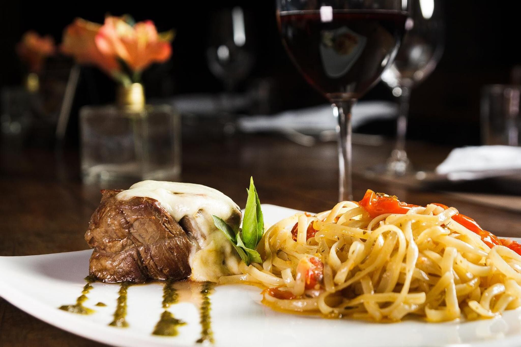 A plate of food with a steak and pasta, accompanied by a glass of red wine.