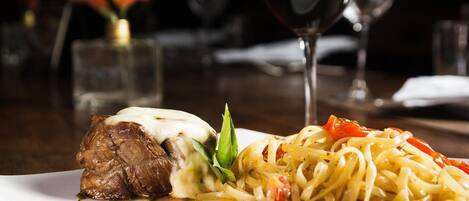 A plate of food with a steak and pasta, accompanied by a glass of red wine.