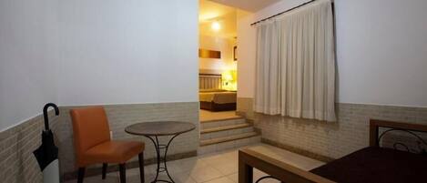 A small, cozy room with a bed, a table, and a chair. There is a staircase leading to an upper level.