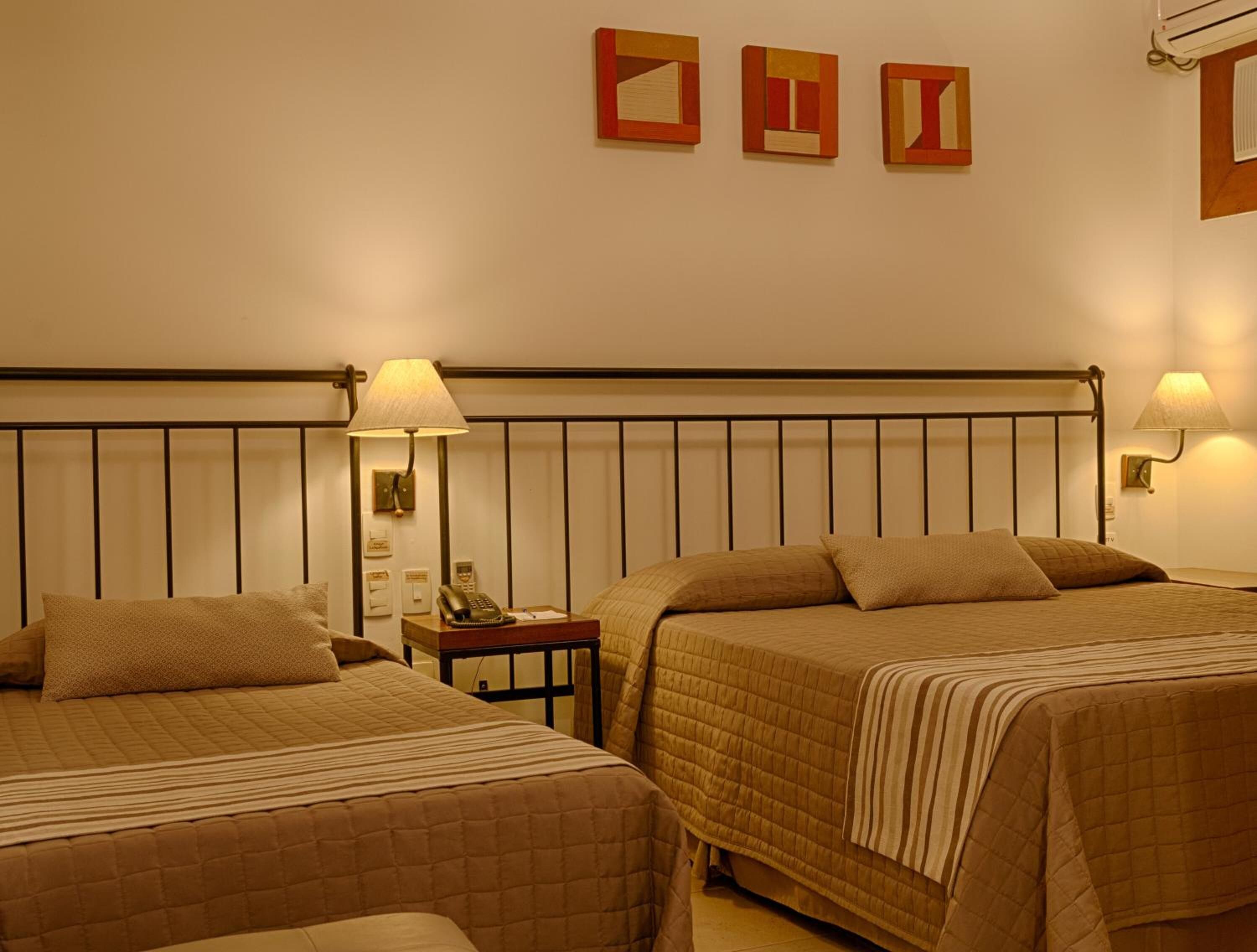 A hotel room with two beds, a nightstand, a lamp, and a wall-mounted phone.