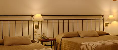A hotel room with two beds, a nightstand, a lamp, and a wall-mounted phone.