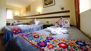 A hotel room with two beds, each with a colorful floral bedspread, a nightstand with a vase of flowers, and a painting on the wall. - Samay Inka Inn (Cusco)
