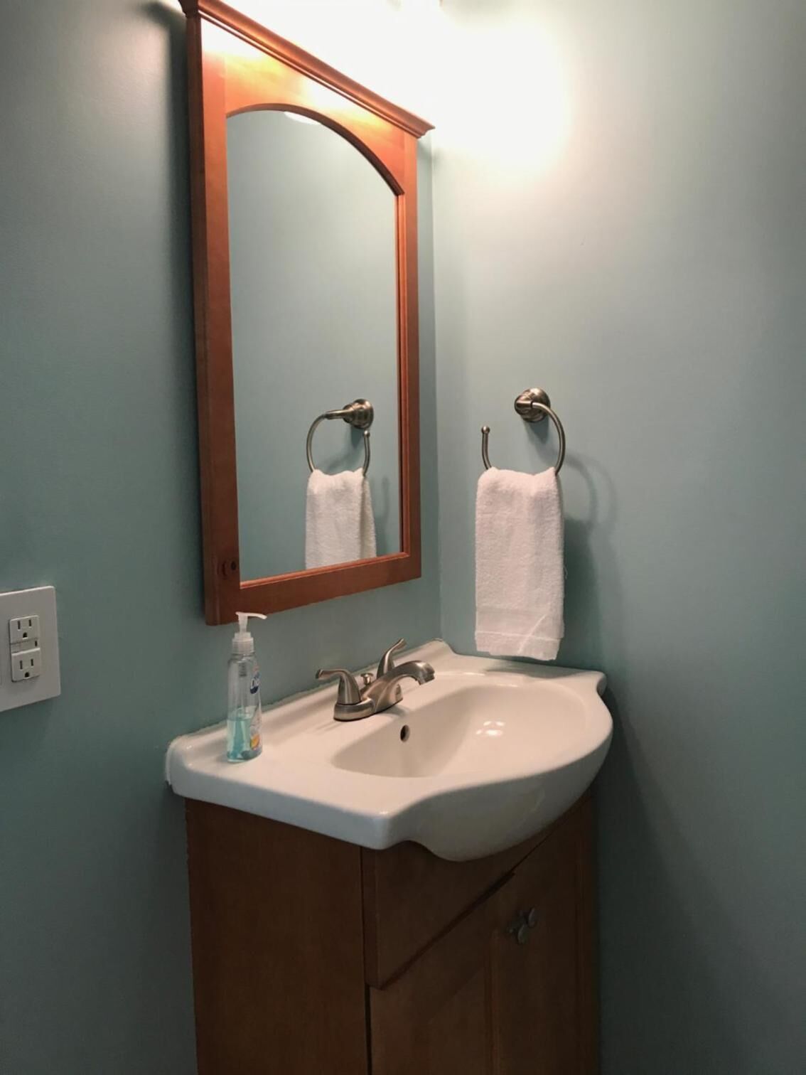 A bathroom with a white sink, a mirror, and two towels hanging on towel rings.