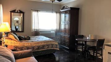 Quarto com cama, escrivaninha, cadeira, guarda-roupa, ventoinha no teto e ar condicionado.