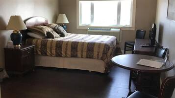 A bedroom with a bed, bedside lamps, a desk with a chair, a ceiling fan, and a window.