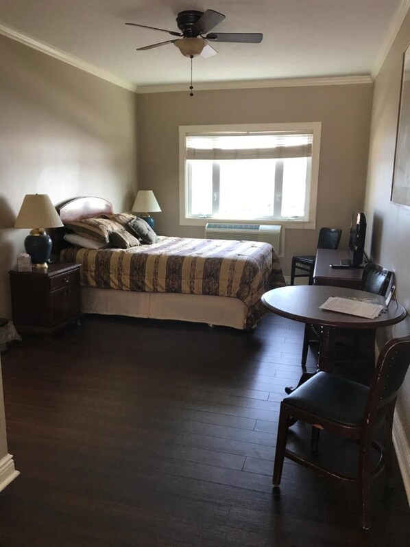 A bedroom with a bed, bedside lamps, a desk with a chair, a ceiling fan, and a window.