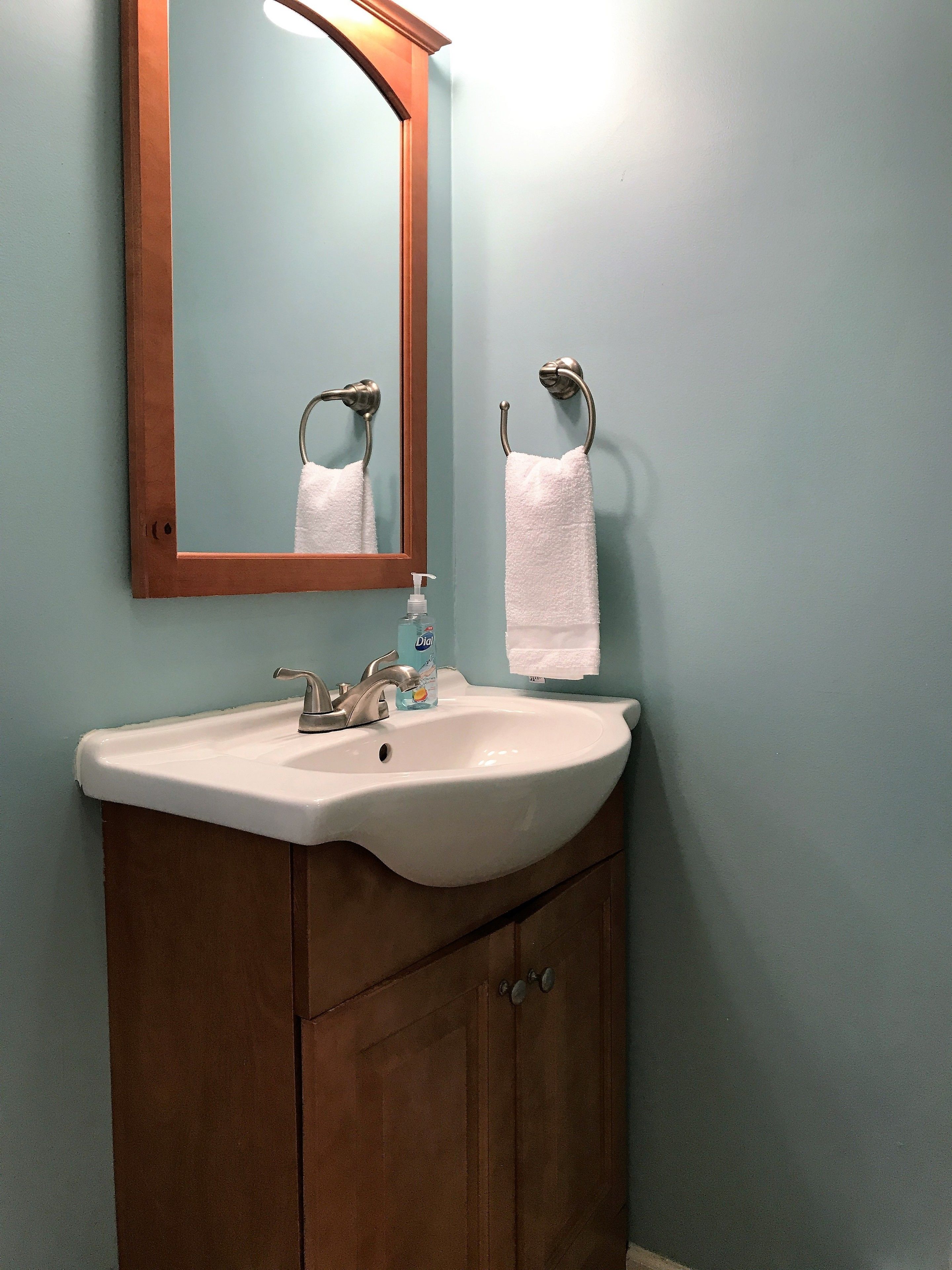 Un baño con lavamanos blanco, tocador de madera, espejo y dos toallas blancas colgadas en ganchos.