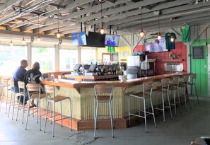 Un espace bar comprenant un comptoir, plusieurs tabourets de bar et un écran de télévision fixé au-dessus du bar.