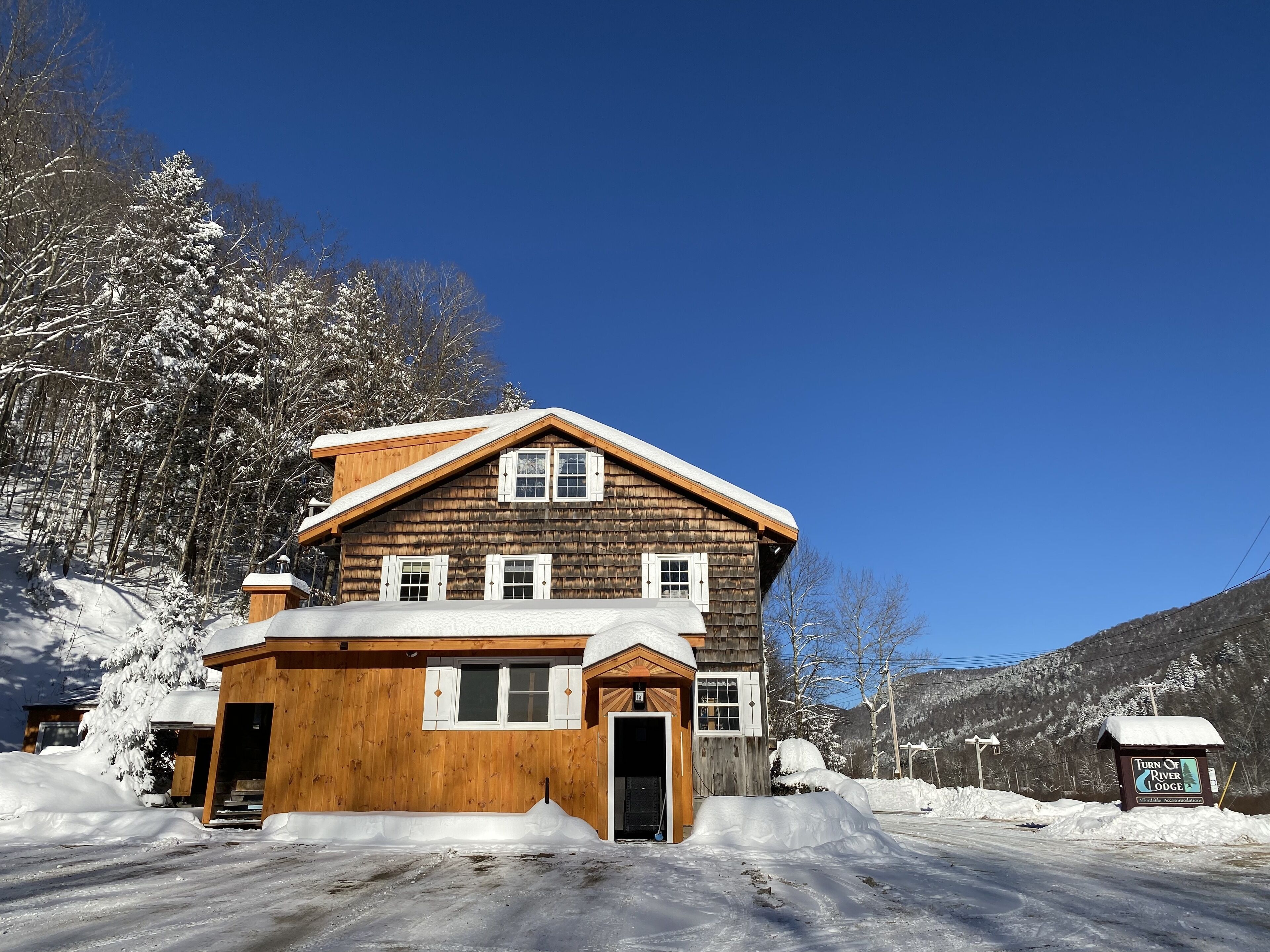 A wooden lodge with a snow-covered roof, a wooden porch, and a sign indicating it is a lodge.