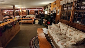 Ett mysigt rum med en varm och inbjudande belysning, träpanel på väggarna, en receptionsdisk i trä, en blommönstrad soffa och en julgran.