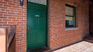 Eine grüne Tür mit einem „Nichtraucher“-Schild, ein kleines Fenster und eine Backsteinwand.