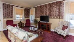 Ein Wohnzimmer mit Fernseher, zwei Sesseln, einer Couch, einem Glastisch und einem Kamin.