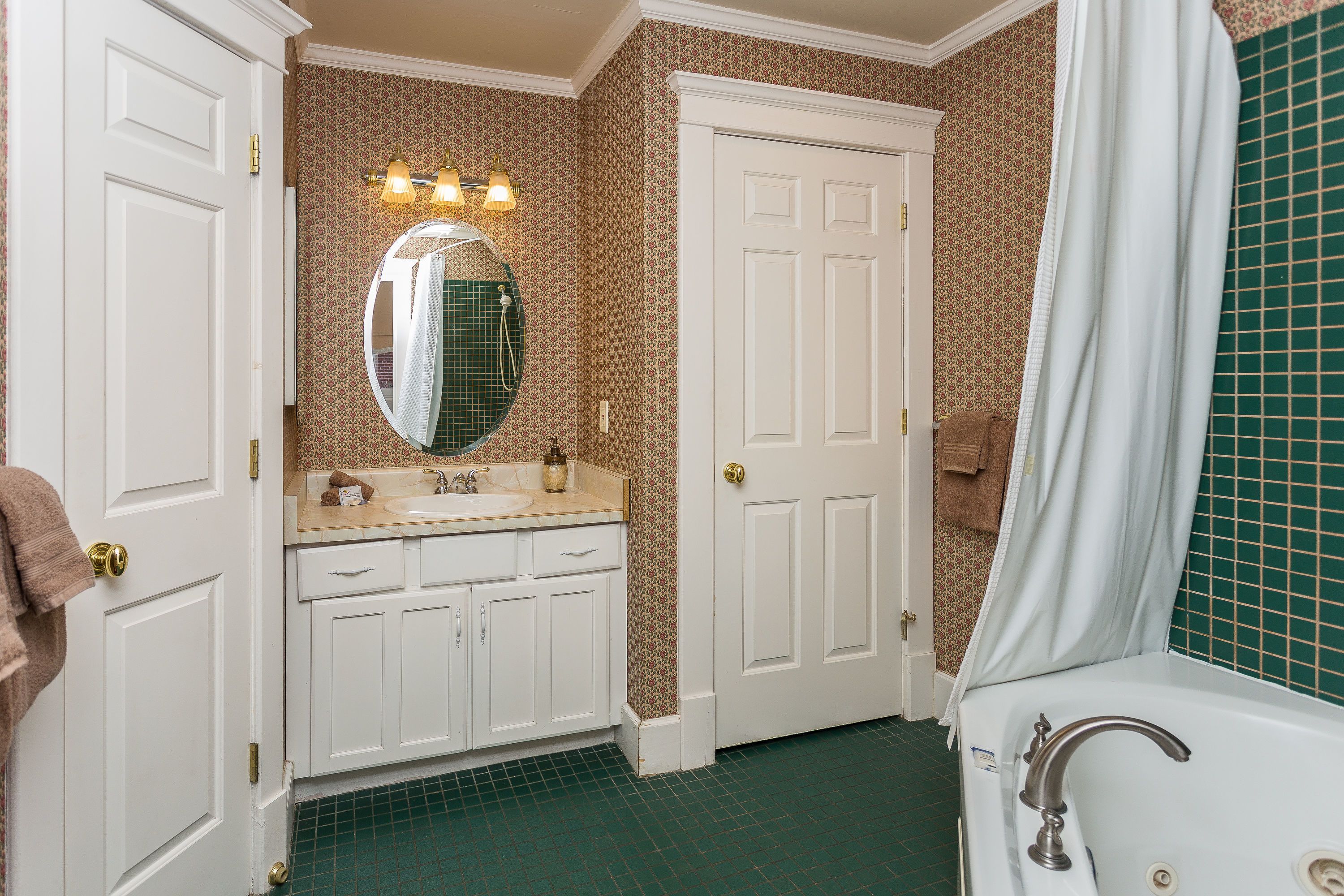 Une salle de bain avec un meuble-lavabo blanc, un miroir rond, une baignoire et un rideau de douche.