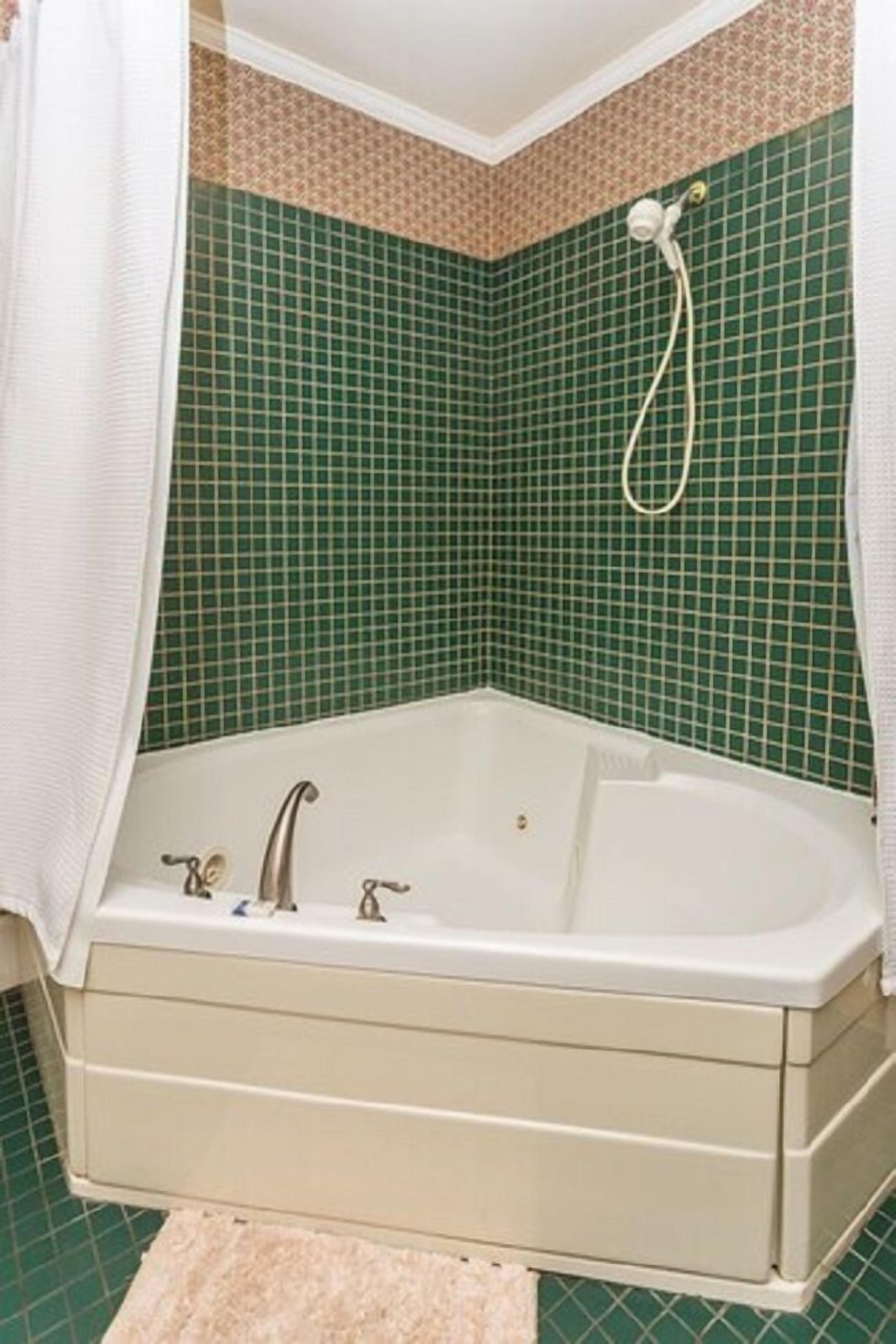 Un baño con bañera, paredes de azulejos verdes y cortina de ducha blanca.