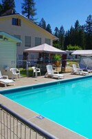 Piscina com espreguiçadeiras e guarda-sóis, cercada por uma grade e um edifício com garagem.