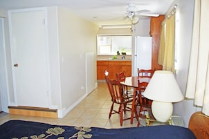 Quarto com cama, mesa de jantar e cadeiras, ventoinha no teto e janela com cortinas.