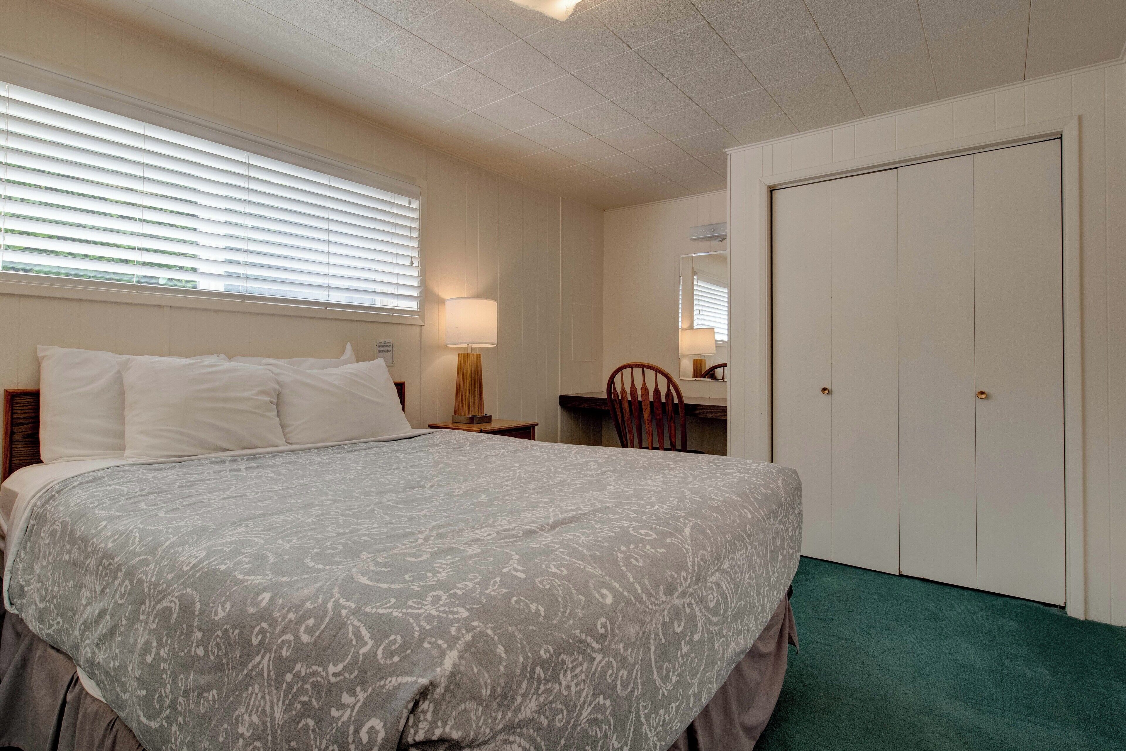 A bedroom with a bed, a desk, a chair, a wardrobe, and a window with blinds.