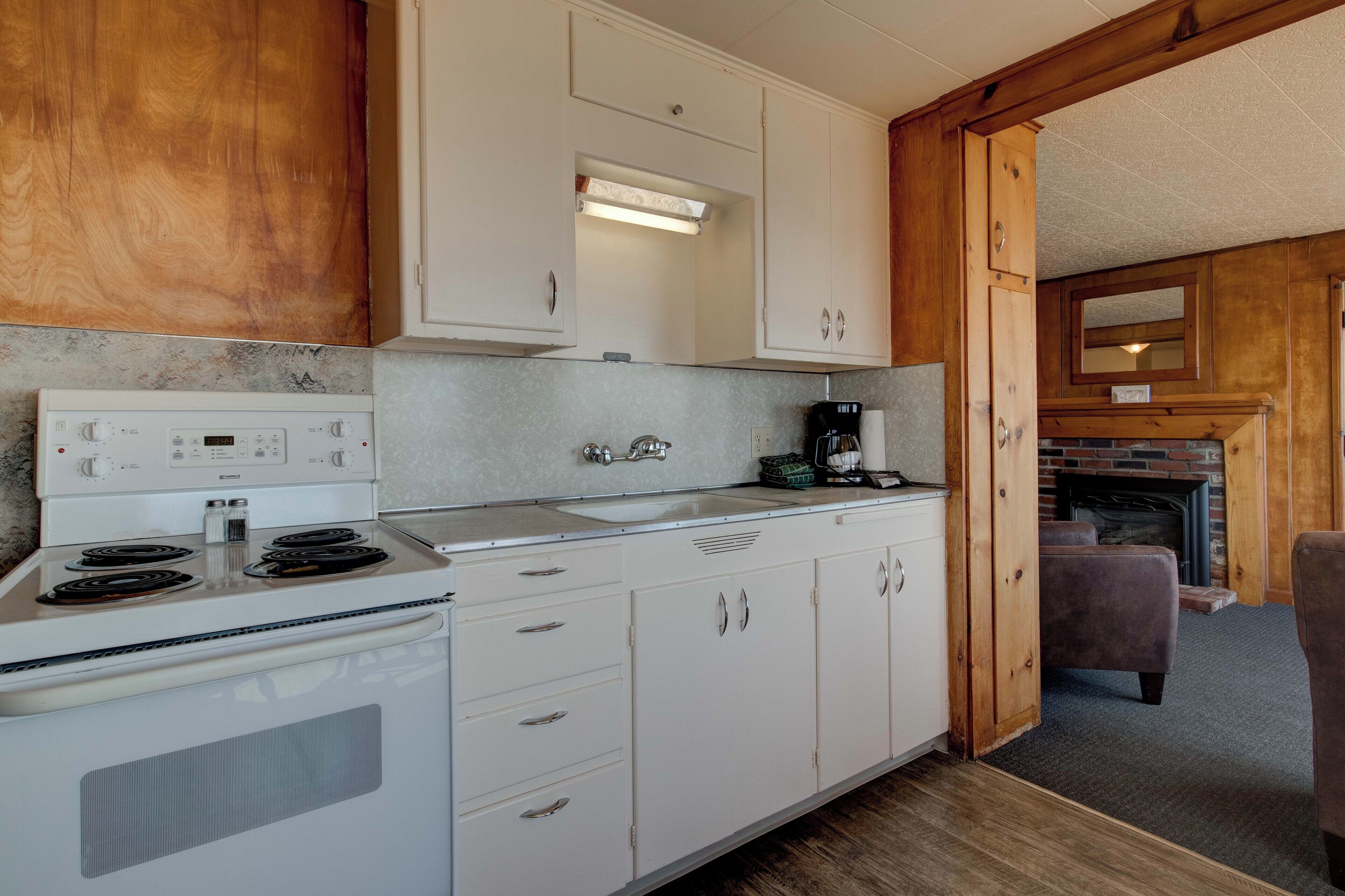 A compact kitchen with white cabinets, a stove, and a coffee maker.