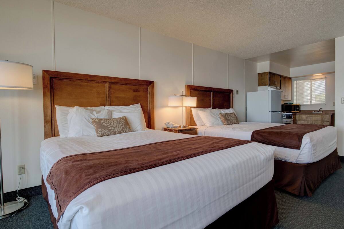 A hotel room with two beds, a kitchenette, and a bathroom.