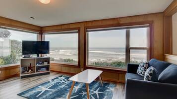 Sala de estar com televisão, mesa pequena e sofá com vista para a praia.