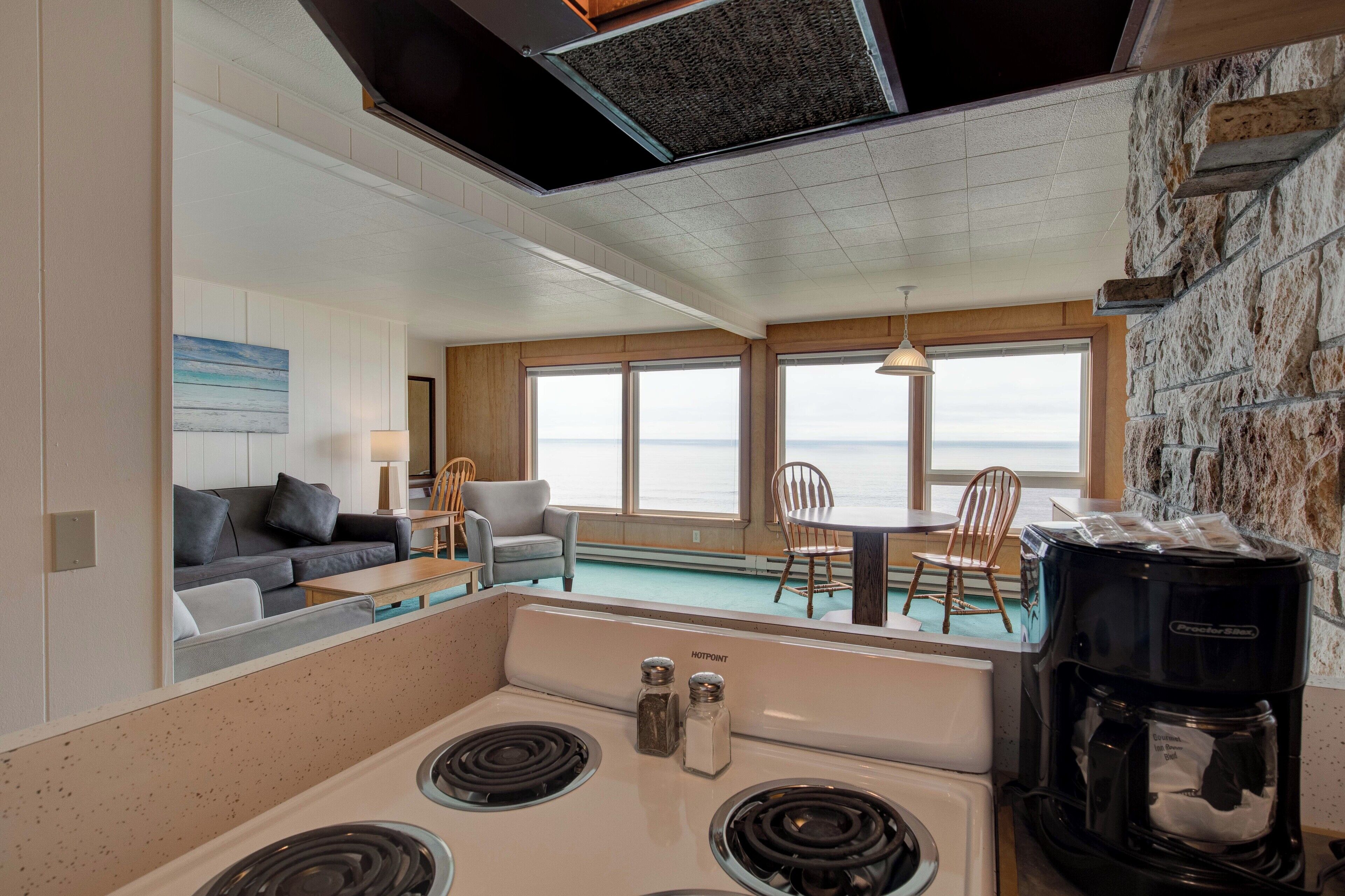 A modern kitchen with a central island, a coffee maker, and a view of the ocean through large windows.