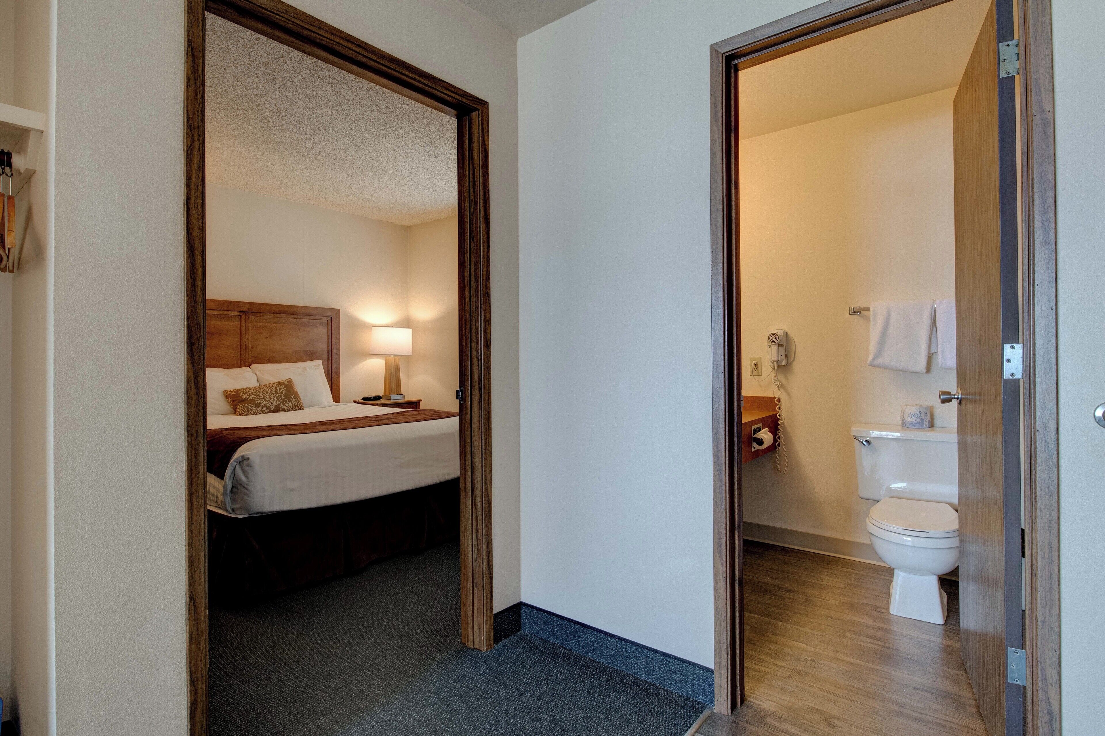A hotel room with a bed, bedside lamp, and a bathroom with a toilet and towel rack.