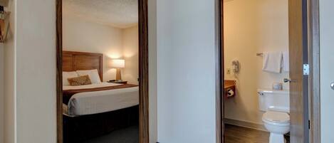 A hotel room with a bed, bedside lamp, and a bathroom with a toilet and towel rack.