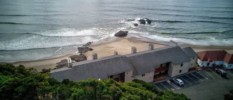 Un edificio frente al mar con estacionamiento, acceso a la playa y vegetación circundante.