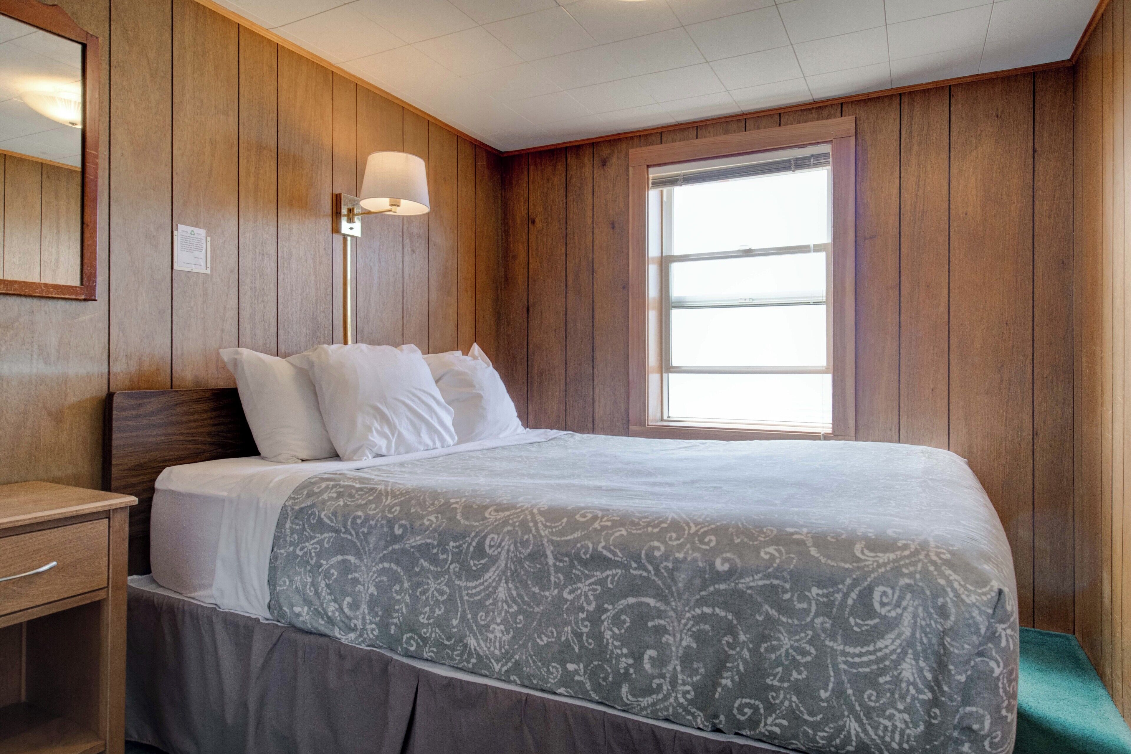 A neatly made bed with a patterned bedspread, a bedside lamp, and a window with blinds.
