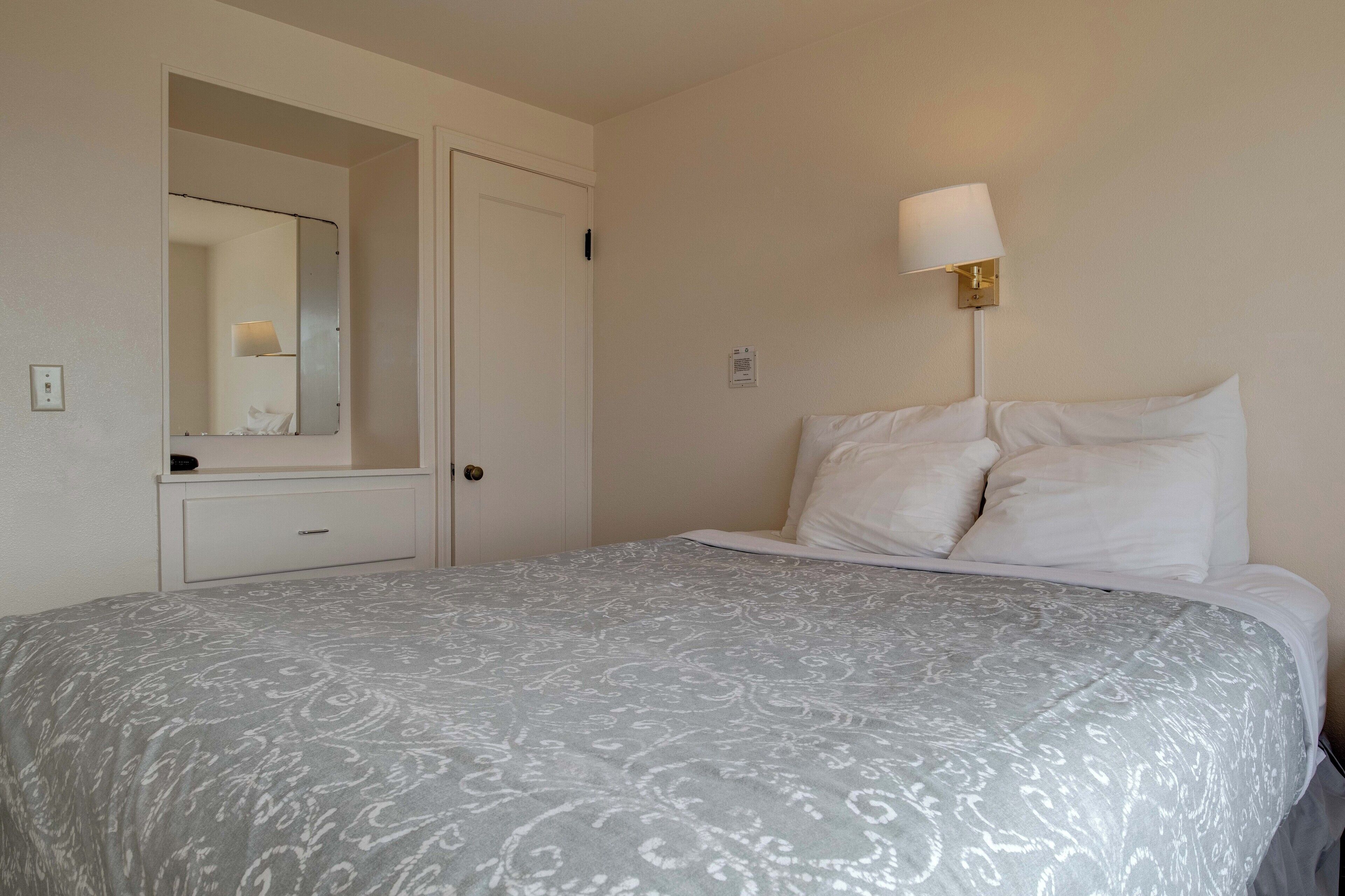Un lit bien fait, recouvert d’une couvre-lit à motifs, une lampe de chevet et un miroir au-dessus d’une commode.