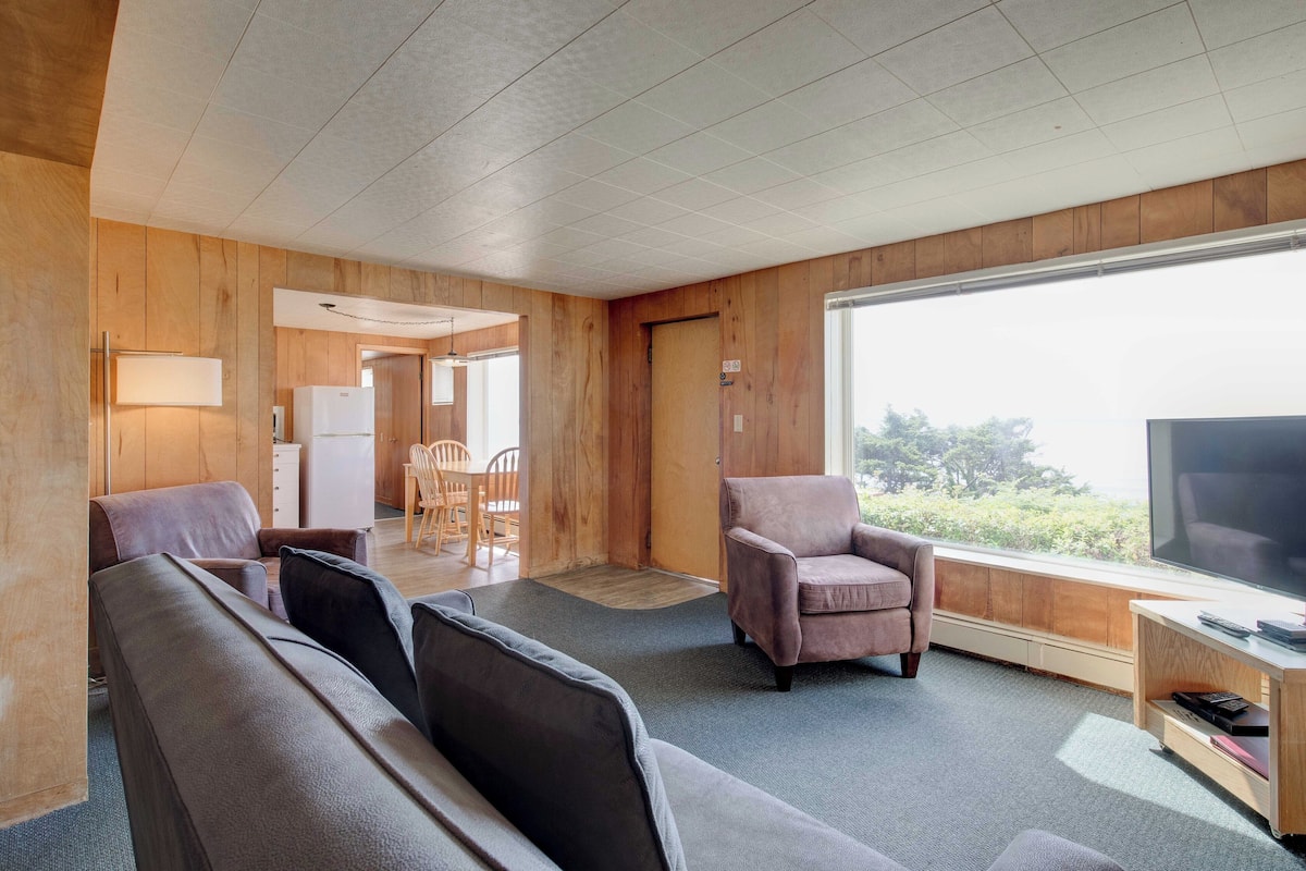 A modern room with a large window, a sofa, a chair, a TV, and a small table.