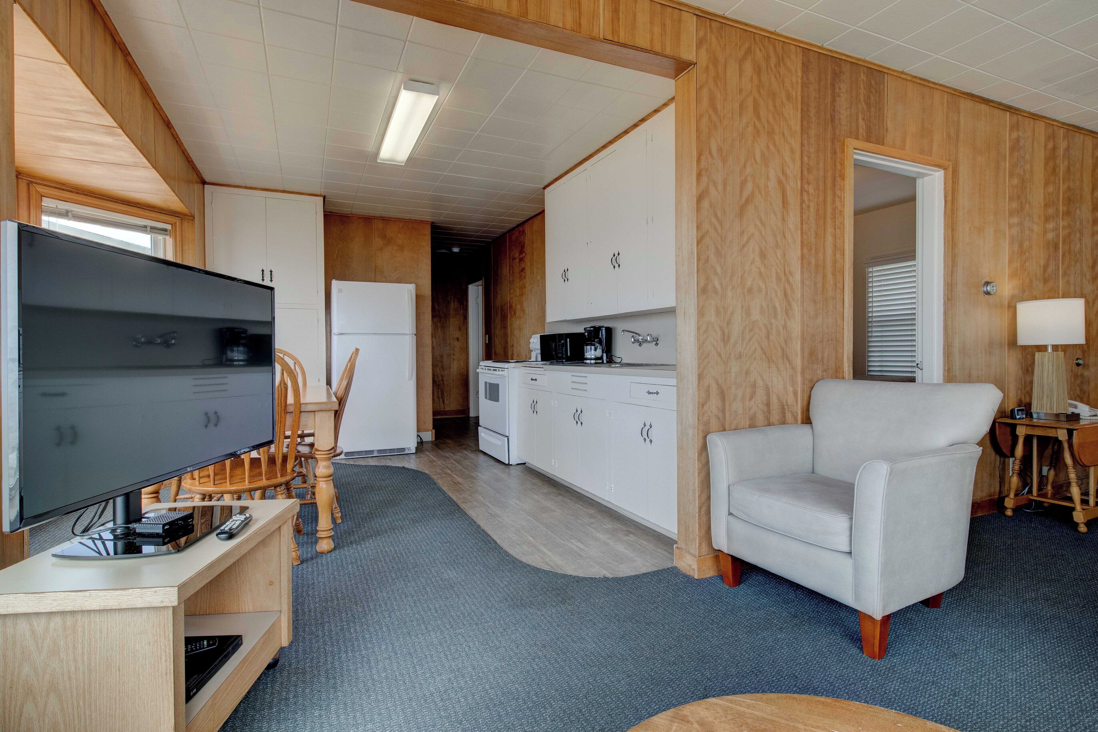 A compact living space with a television, a sofa, a kitchen area, and a dining table.